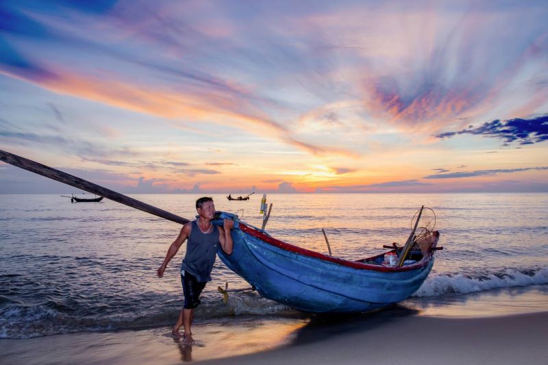 Pêcheur de Quảng Bình, Vietnam, réparant ses filets sur une plage au lever du soleil, illustrant la vie quotidienne des communautés de pêcheurs locales